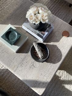 a coffee table with flowers and books on it, along with a vase filled with white roses