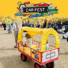 a small red cart with people standing around in the background and a sign that says carfest on it