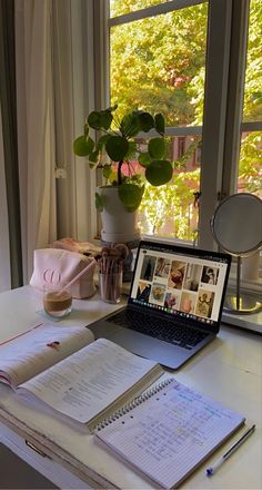 an open laptop computer sitting on top of a desk next to a book and plant