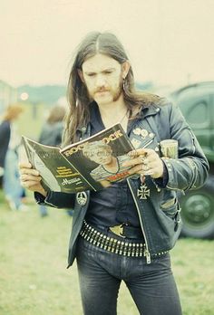 a man with long hair is holding a book and looking down at the pages in his hand