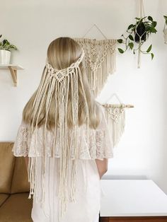 a woman standing in front of a wall hanging with macrame and plants on it