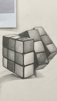 a pencil drawing of a cube sitting on top of a white table next to a piece of paper