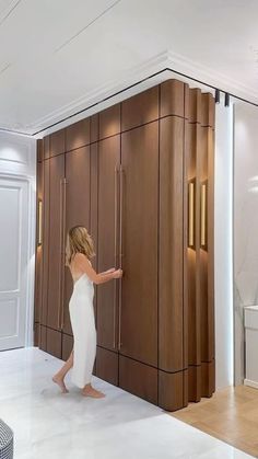 a woman in a white dress is opening the door to a bathroom with wooden cabinets