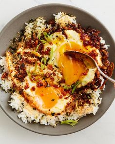 an egg on top of rice in a bowl with a spoon next to some other food