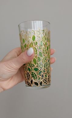 a hand holding a glass with gold and green designs on the outside, in front of a gray background