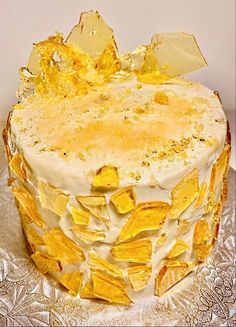 a cake with yellow frosting and gold leaf decorations on it's top, sitting on a silver platter