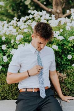 a young man is sitting on the ground tying his tie and looking at his watch