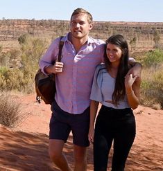 a man and woman are walking in the desert with their arms around each other as they pose for a photo