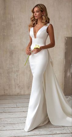 a woman in a white wedding dress holding a flower and posing for the camera with her hand on her hip