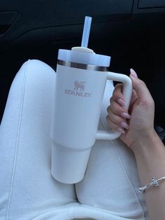 a woman holding a white coffee cup on top of a seat in the back of a car