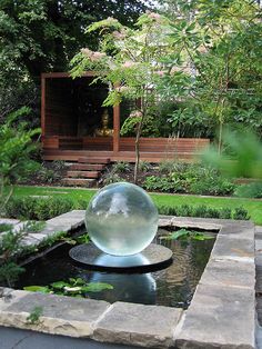 a glass ball sitting on top of a pond in the middle of a garden area