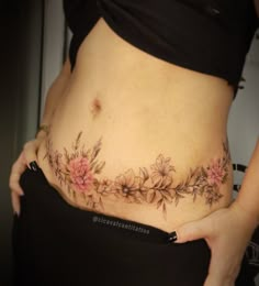 a woman's stomach with pink flowers on the side, and her belly tattoo