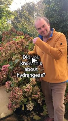 a man is standing in front of some flowers and pointing at the camera with his finger