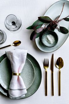 a place setting with silverware, napkins and gold utensils on a white table cloth