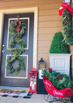 two christmas wreaths on the front door of a house with decorations around them and a red sleigh