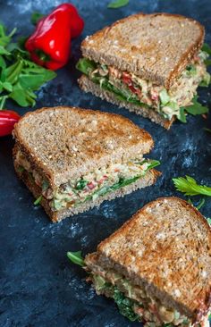 three sandwiches cut in half on top of a blue surface next to red peppers and green leaves