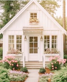 a small white house with lots of windows and flowers in the front yard, along with potted plants