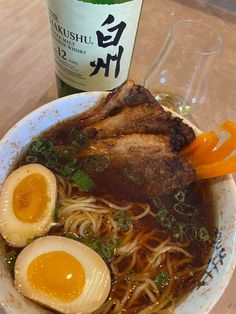 a bowl of ramen with two boiled eggs and chopsticks next to a bottle of wine