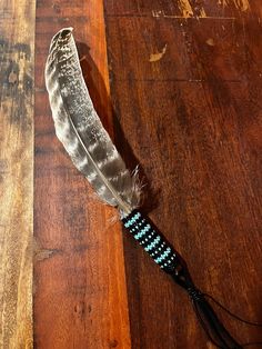 a feather on a wooden floor with beads and feathers attached to the end of it