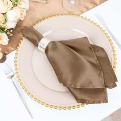 a place setting with napkins, silverware and gold beaded trim on a white plate