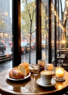 a table with coffee, croissants and bread on it in front of a window