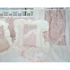 a crib with pink and white bedding, pillows and blankets on top of it