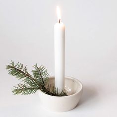 a single candle is lit in a small white bowl with a pine branch on it