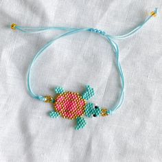 a beaded bracelet with a pink and blue turtle on it's side, sitting on a white sheet