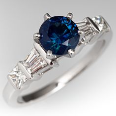 This beautiful ring is centered with one (1) round brilliant cut natural sapphire weighing 1.30 carats that is set into a six-prong head. The shoulders of the ring are each accented with two (2), channel set, tapered baguette cut diamonds and one (1), channel set, princess cut diamond. The ring measures 7.9mm at the top, rises 8.5mm above the finger, tapering to 1.8mm wide and 1.2mm thick at the base of the shank. This ring is currently a size 6.75. Classic Sapphire Diamond Ring Gia Certified, Classic Gia Certified Sapphire Ring, Luxury Diamond Ring With Brilliant Cut Lab-created Sapphire, Classic Sapphire Diamond Ring With Brilliant Cut, Gia Certified Sapphire Diamond Ring In Timeless Style, Dazzling Brilliant Cut Sapphire Ring In Platinum, Dazzling Sapphire Ring With Brilliant Cut, Luxury Lab-created Sapphire Ring With Prong Setting, Gia Certified Timeless Sapphire Diamond Ring