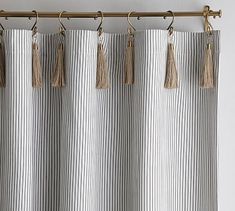 a curtain with tassels hanging from it's metal rod, in front of a white wall