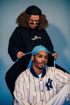 two people sitting on top of each other in front of a blue background with one person cutting another persons hair