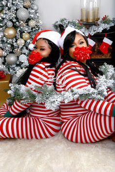 two women dressed in red and white striped pajamas sitting on the floor next to a christmas tree