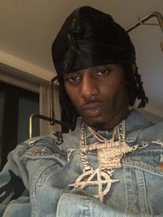 a young man wearing a denim jacket and a black bandana is looking at the camera