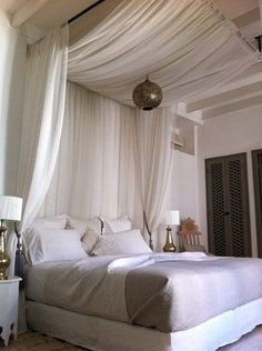 a bed with white drapes and pillows on it