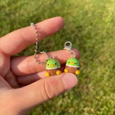 a person holding two tiny green birds on a chain necklace in their left hand, with grass in the background