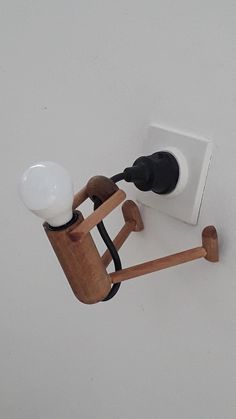 a wooden object with a light on it's side hanging from the ceiling in front of a white wall