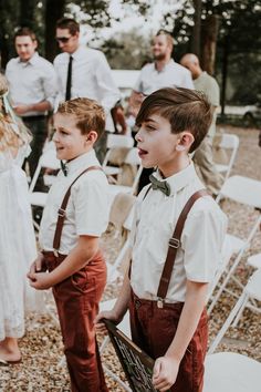 two young boys in suspenders and bow ties standing next to each other at an outdoor wedding