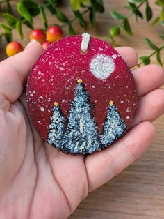 a hand holding a red ornament with trees on it