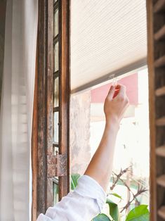 a woman standing in front of a window with her hand up to the sky and looking out