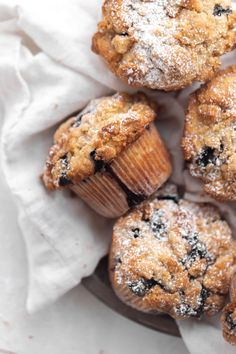 some blueberry muffins are sitting on a white napkin and it is covered in powdered sugar