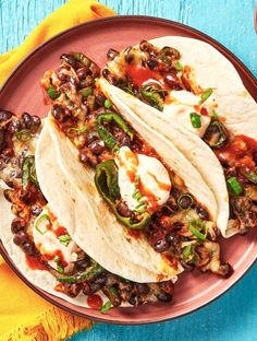 three tacos on a pink plate with green peppers and black beans in the middle