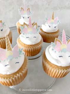 cupcakes with white frosting and unicorn faces on them sitting on a glass plate