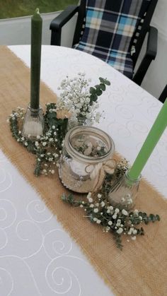 two candles sitting on top of a table next to some flowers and plants in jars