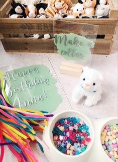 there is a small white teddy bear next to two bowls of confetti and marshmallows