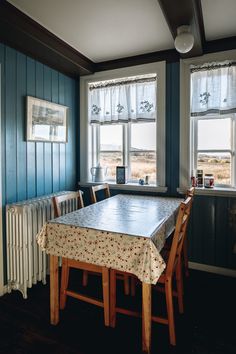 a dining room table and chairs in front of two windows with blue paneled walls