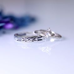 two wedding rings sitting next to each other on top of a white table with blue flowers in the background