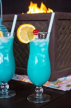 two glasses filled with blue liquid next to each other on a table in front of a fire place