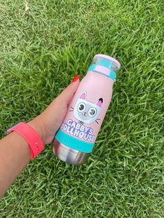 a person holding onto a pink and blue water bottle in the grass with an image of a cat on it