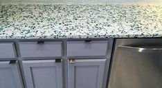 a kitchen counter with blue and white speckles on the top, next to a silver dishwasher