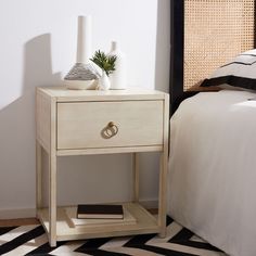 a white nightstand with a book and vase on it next to a black and white bed